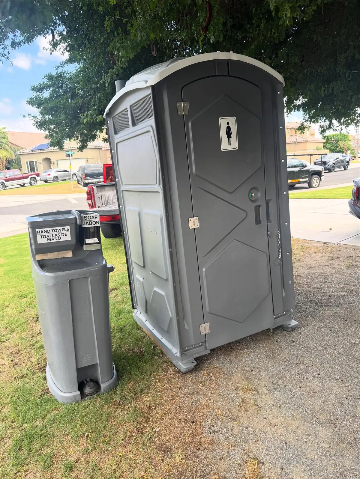 Grey porta potty and a hand washing station set up on a front lawn