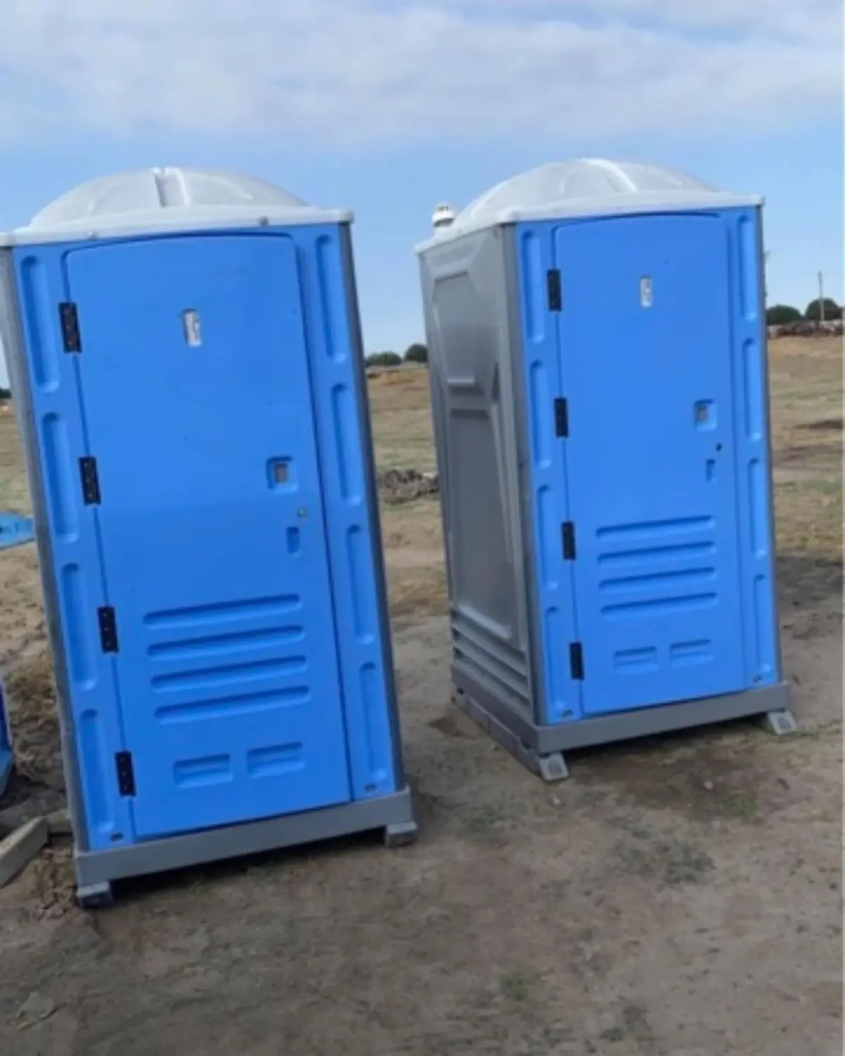 Two blue standard porta potties set on open ground