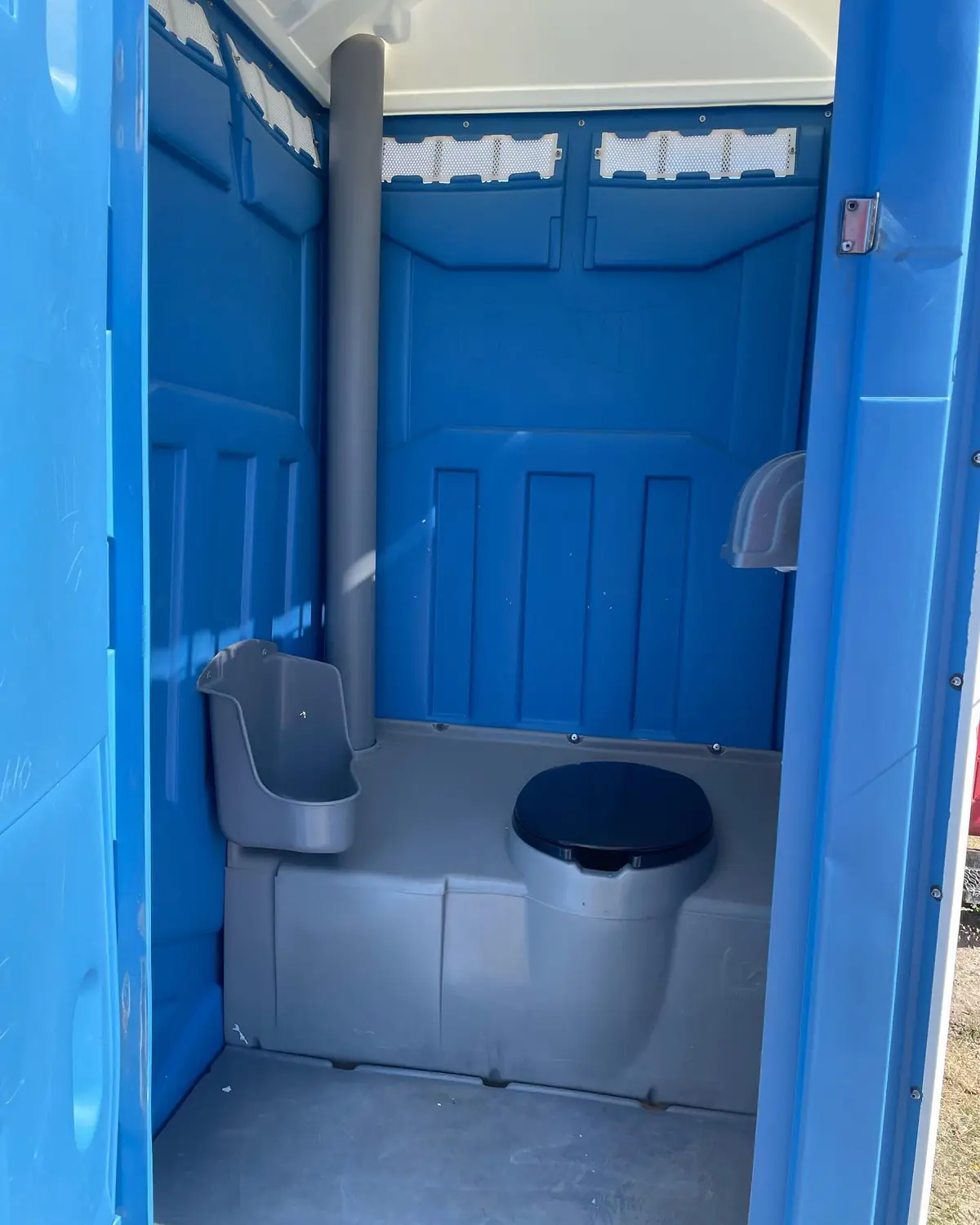 Inside a blue standard porta potty with a seat, urinal and sanitizer